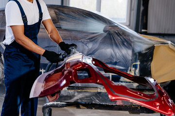 Unrecognizable mechanic using grinding unit on red bumper at automobile repair and renew service station.