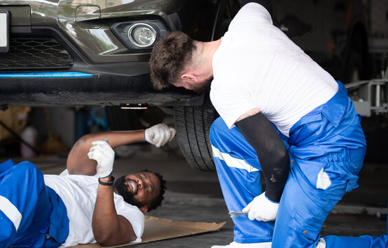 Bothe of car mechanic working in an auto repair shop, Check the operation of the engine of under the car that comes in for repairs at the auto repair shop.