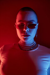Vertical closeup portrait of empowered young woman with buzzcut wearing futuristic sunglasses in...