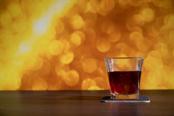 Glass of whiskey on the bar in front of the blur image Christmas background. Festive abstract background with bokeh defocused lights and stars