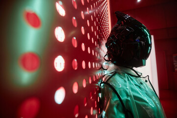 Futuristic side view portrait of person wearing black robot mask against red, copy space