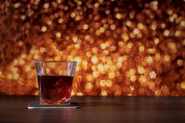 Glass of whiskey on the bar in front of the blur image Christmas background. Festive abstract background with bokeh defocused lights and stars