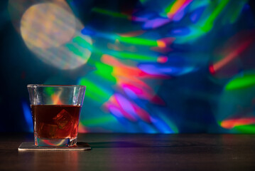 Glass of whiskey on the bar in front of the blur image Christmas background. Festive abstract background with bokeh defocused lights and stars