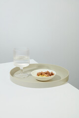 The pills are displayed on a white ceramic plate. A glass of water is placed on a round ceramic dish on a white table. Space for medicine advertising.