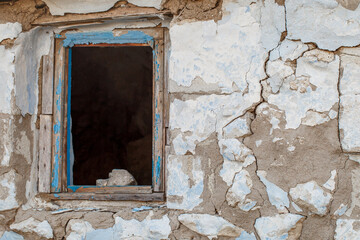 Window without glass with broken frame on peeling wall of old ruined house