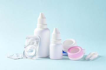 Obraz na płótnie Canvas Contact lenses, solution bottle and eye drops with accessories on blue background