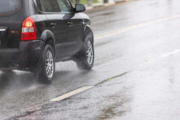 rain water splashing flows from wheels of black SUV that moving fast on asphalt road - obrazy, fototapety, plakaty
