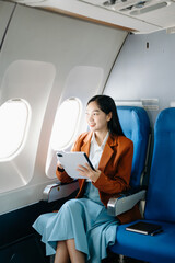 Asian executive excels in first class, multitasking with digital tablet, laptop. Travel in style, work with grace..