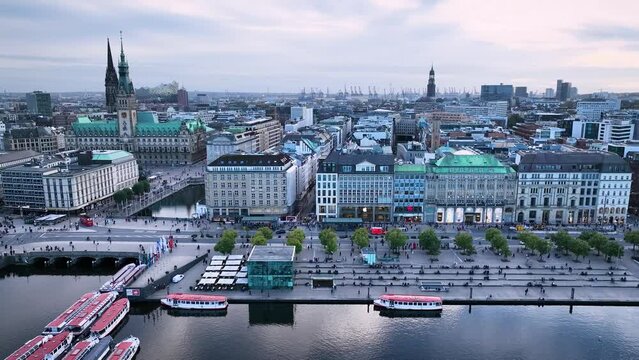 Aerial footage of Hamburg's Alster Lake, Alsterarkaden and Jungfernstieg, surrounded by the impressive backdrop of the iconic Hamburg skyline and the bustling urban life.
