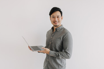 Asian man with beard wear grey shirt using and holding laptop, presenting notebook with happy smiling face, looking at camera and standing isolated over white background wall.