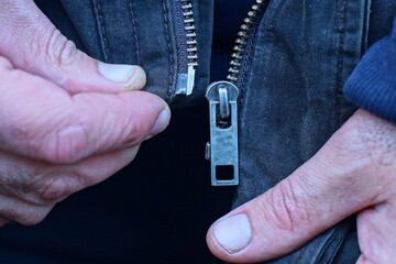 fastening with two hands an iron old industrial zipper in a stylish classic fashionable brown fabric warm autumn jacket on the street during the day © FEDOR