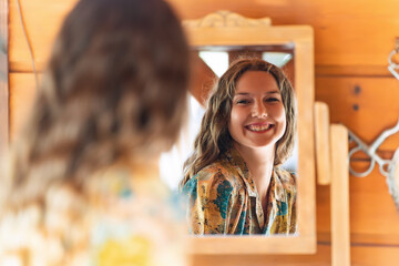 Young woman smiling while looking herself in a mirror at home. - obrazy, fototapety, plakaty