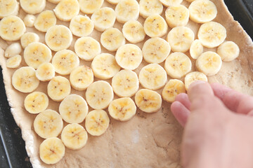 Hand placing round banana pieces on dough on baking sheet, preparing banana pie