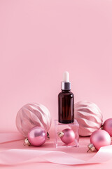 A cosmetic bottle with a dropper with facial skin care product stands on a transparent cube podium among New Year's pink balloons. Vertical view.