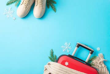 Winter vacation concept. Overhead view of a red suitcase, cozy boots, knitted scarf, fir branches,...