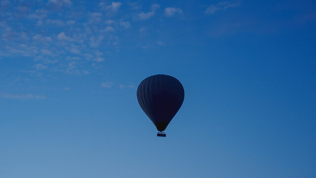 A hot air balloon with people floats in the dark sky, just before dawn.