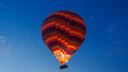 Naklejka premium A colorful balloon in the clear dark sky at dawn, with fire burning inside, and people in the basket expressing joy.