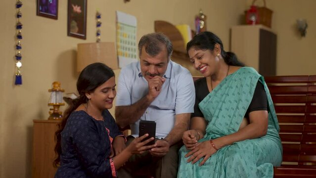 Indian teenager daughter showing Mobile phone app to middle aged parents at home - concept of social media sharing, Internet or technology and family bonding
