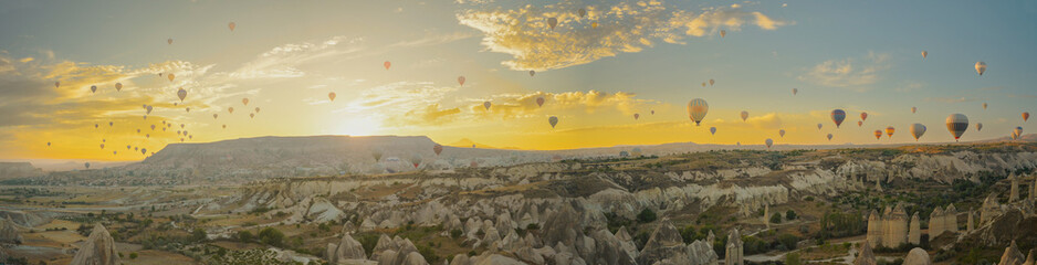 A vast number of hot air balloons in Cappadocia, with the sun about to rise behind the mountains. Golden clouds create a breathtaking panorama.
