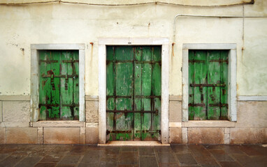 Fototapeta na wymiar Shabby wall with windows and a green wooden door in Italy on the island of Chioggia