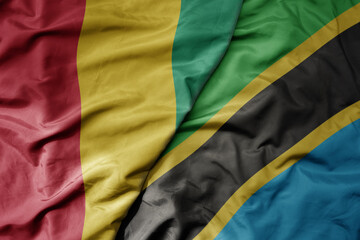 big waving national colorful flag of guinea and national flag of tanzania .