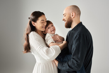 cheerful mother in white dress hugging her little son while her husband looking at them, family