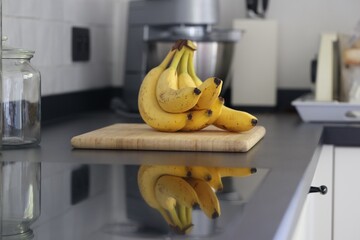 A portrait of a bunch of yellow bananas lying on a wooden cutting board on a black kitchen...