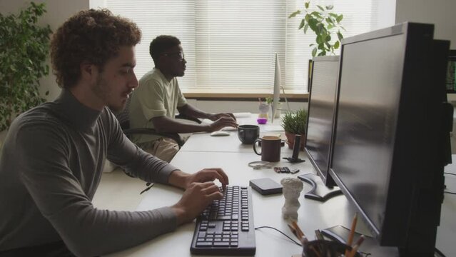 Waist up of two diverse young male programmers working on desktop computers in contemporary open space office