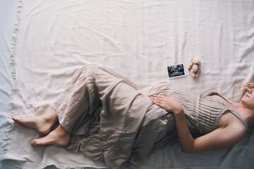 Pregnant woman in dress holding hands on belly lying on side in profile in bed.  Expectant mother...