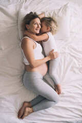 Pregnant mother and daughter resting in bed. Young woman with her first child during second pregnancy. Motherhood and parenting concept.