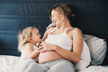 Pregnant mother and daughter resting in bed. Young woman with her first child during second pregnancy. Motherhood and parenting concept.