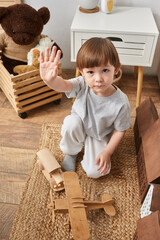 vertical shot of adorable little boy playing with wooden toys and waving hi at camera, family