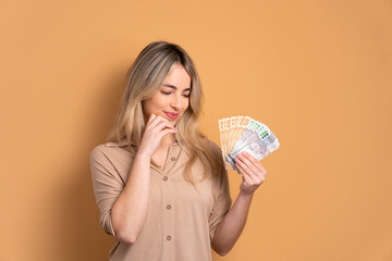 interested young woman looking at brazilian money cash in beige studio background. financial, credit, purchase, rich concept. 