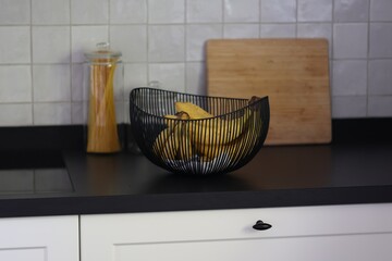 A portrait of a bunch of bananas lying in a decorative black metal bowl on a black kitchen counter....