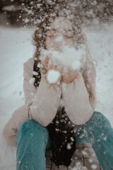beautiful young girl playing with white snow in the winter forest