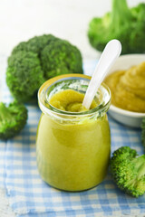 Green broccoli baby food in white bowl and jar on table. Green baby food. Child first feeding concept. Baby Natural Food. Production and menu of baby food. Selective focus.