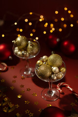 Two beautiful champagne glasses are filled with shiny toys on red background. Serpentine and lights. Holidays content.