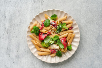 Wholegrain pasta penne with broccoli and red grilled bell pepper and on light grey slate, stone or concrete background. Vegan pasta. Traditional Italian cuisine. Flat lay. Copy space