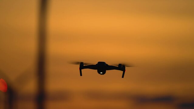 Drone flying against Windmill turbine park with rotating blades generating green energy, silhouette quadrocopter uses for study advantages and drawbacks of electric station at amazing cloudy colorful