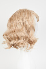 Naklejka premium Natural looking blonde fair wig on white mannequin head. Middle length hair cut on the plastic wig holder isolated on white background, side view.