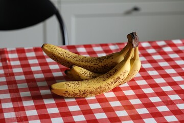 A closeup portrait of yellow bananas with some brown spots lying on a red and white table cloth on...