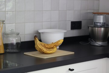 A portrait of a bunch of yellow bananas lying on a white plastic cutting board on a black kitchen countertop. The delicious energizing food is ready to eat and ideal before sport.