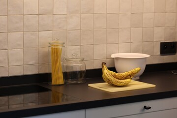 A portrait of a bunch of yellow bananas lying on a white plastic cutting board on a black kitchen countertop. The delicious energizing food is ready to eat and ideal before sport.
