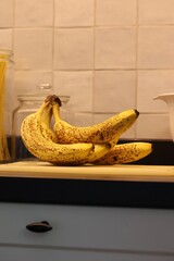 A vertical of a bunch of yellow bananas with brown spots lying on a white plastic cutting board on...