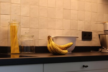 A portrait of a bunch of yellow bananas with som brown spots lying on a black kitchen countertop....