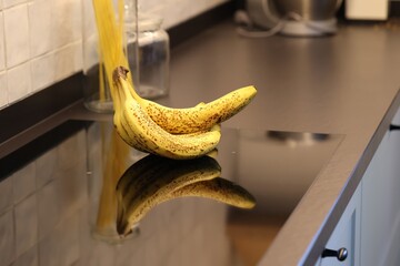 A portrait of a bunch of yellow bananas with some brown spots on a induction stove or cooker in a...