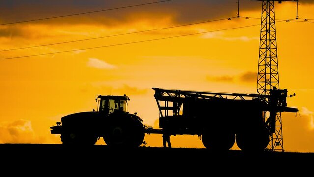 Silhouette unrecognizable man farmer working with powerful tractor after spraying field at mesmerizing colorful cloudy sundown in evening. Working in Agricultural business using modern powerful agro