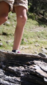A youngster explores the wild, navigating a fallen tree by a mountain lake in a U.S. national park. Zooming in on legs and boots, it encapsulates a childhood immersed in nature, fostering growth 