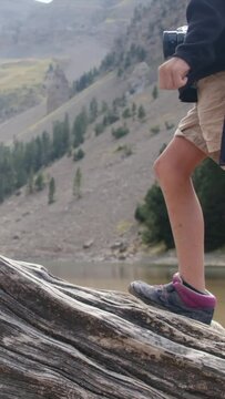 A child balances on a fallen tree by a mountain lake in a U.S. national park. Close-up of legs and boots Adventure, growth, childhood nature connection, eco-education Overcoming challenges and growing