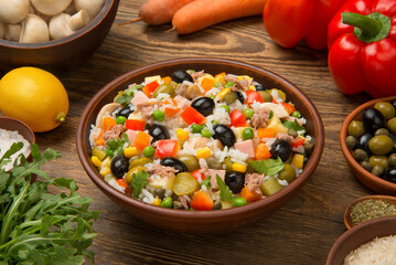 Italian rice salad with tuna in a brown ceramic salad bowl on a rustic wooden table with ingredients. - 679201314